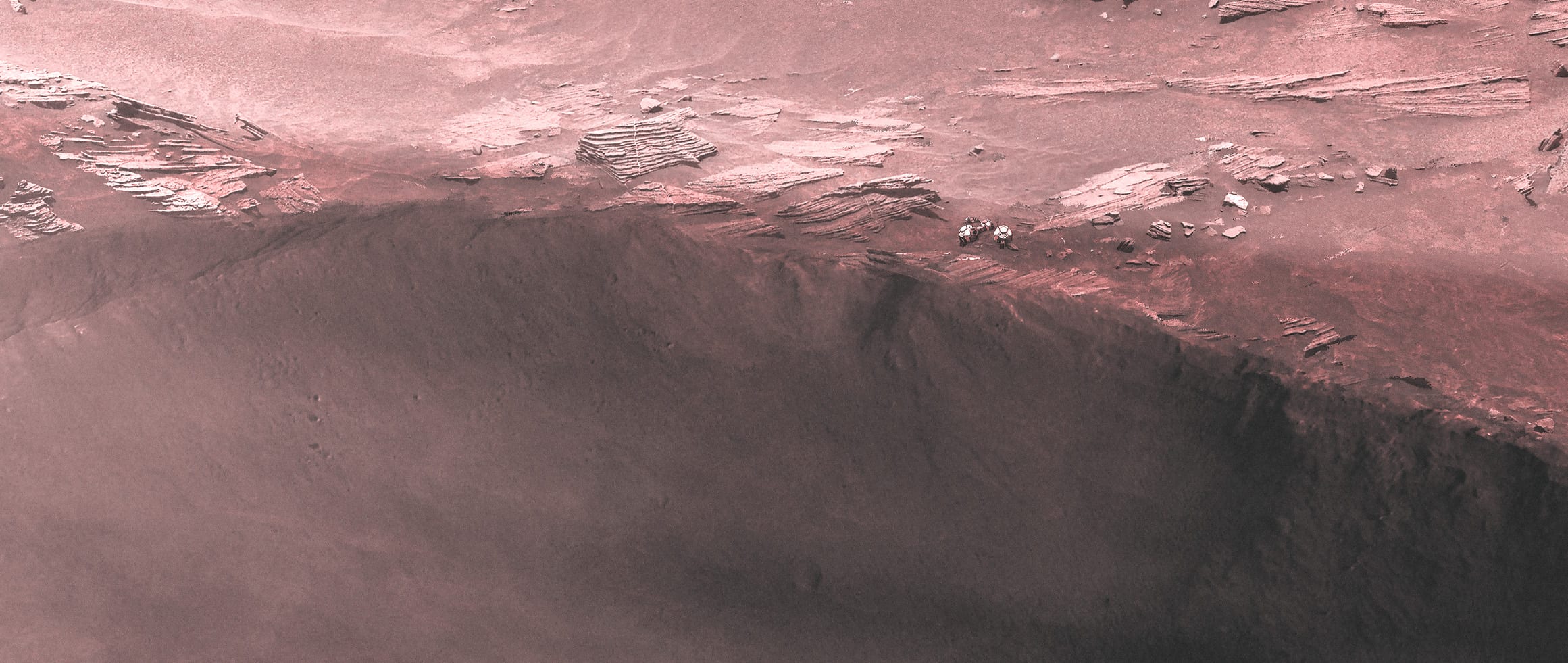 Two tiny explorers at the edge of a vast Martian crater