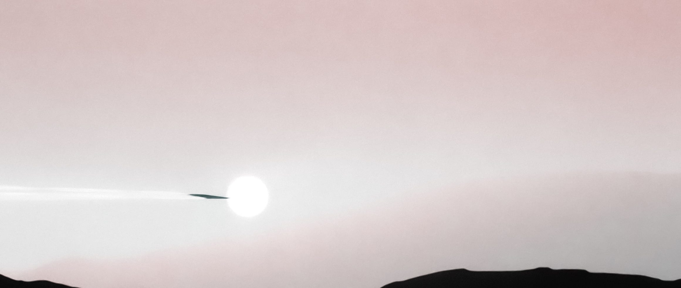 A bright sun crossing a near-white horizon above dark Martian terrain